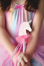 Child holding a Fanciful Unicorn Wand with pink tulle, glittery unicorn, and flowing ribbons in a colorful dress.