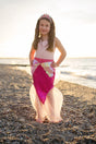 Girl wearing Mermaid Glimmer Skirt Set with Headband | Pink standing on a pebble beach at sunset.