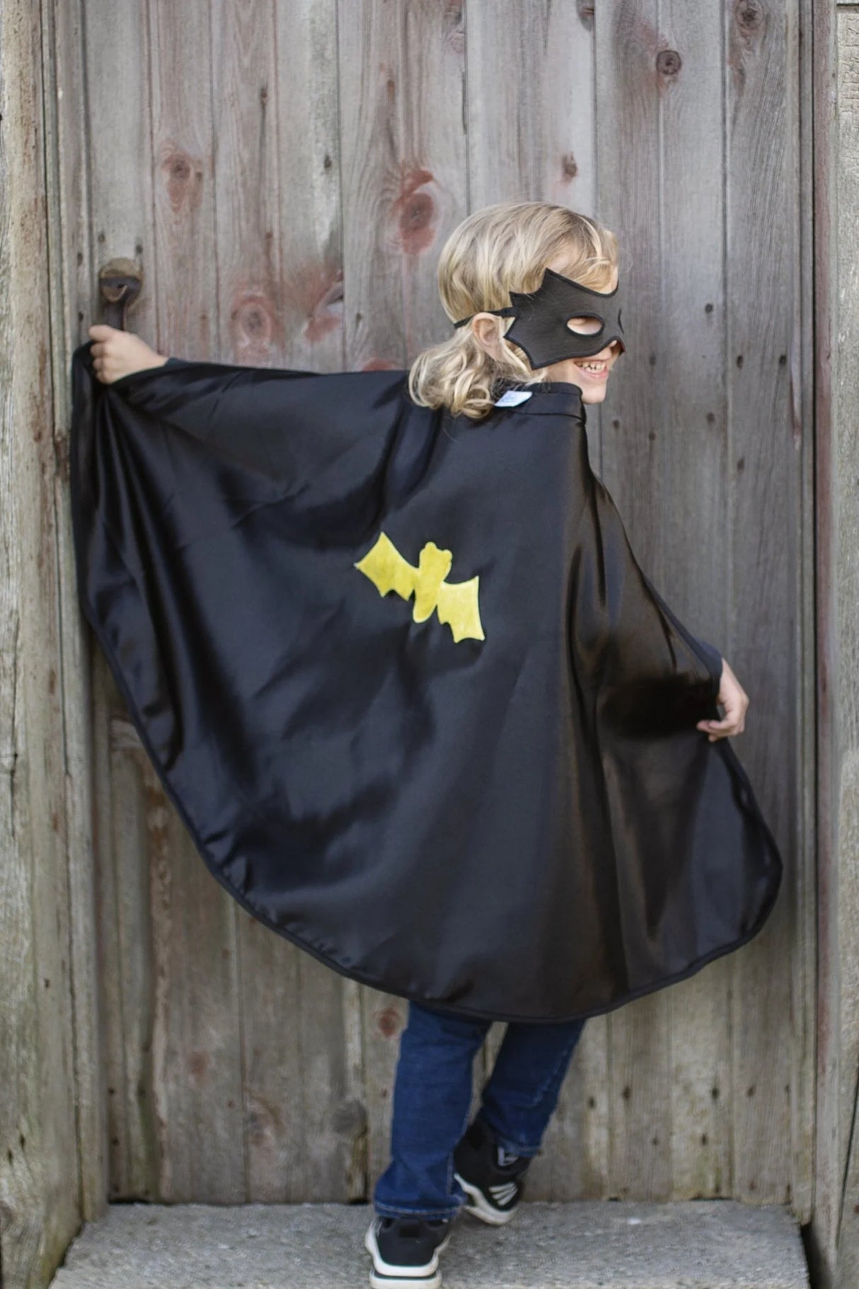Child wearing Spider Bat Reversible Cape & Mask Size 4-6 showing black satin cape with yellow bat emblem outside.