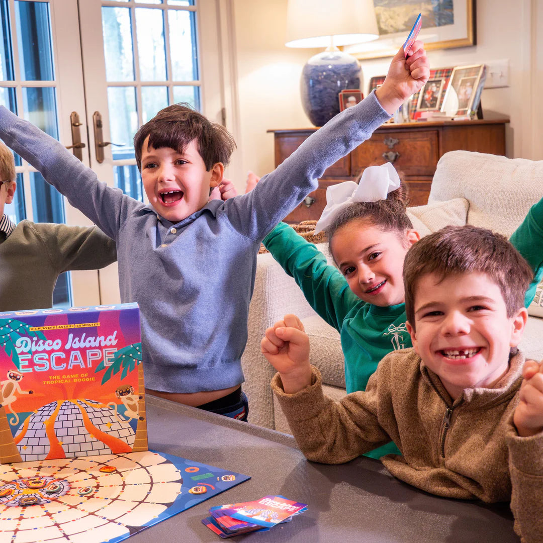 Children celebrating while playing the Disco Island Escape board game on a living room table indoors.