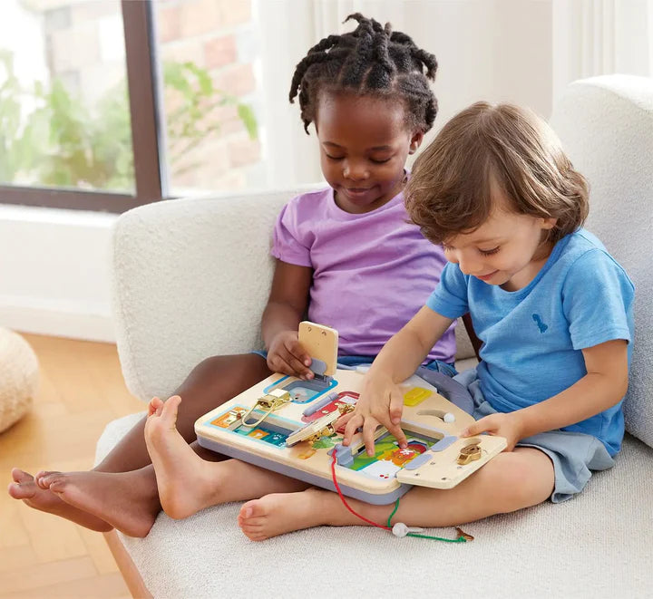Two children sitting on a couch playing with the Lock & Learn Playboard, exploring locks and doors for creative play.