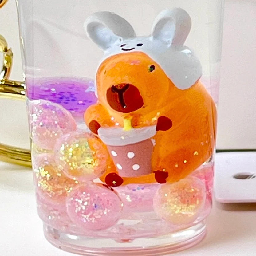 Capybara Boba Floaty Keychain featuring an orange capybara in a bunny hat holding a boba drink with floating glitter bubbles.