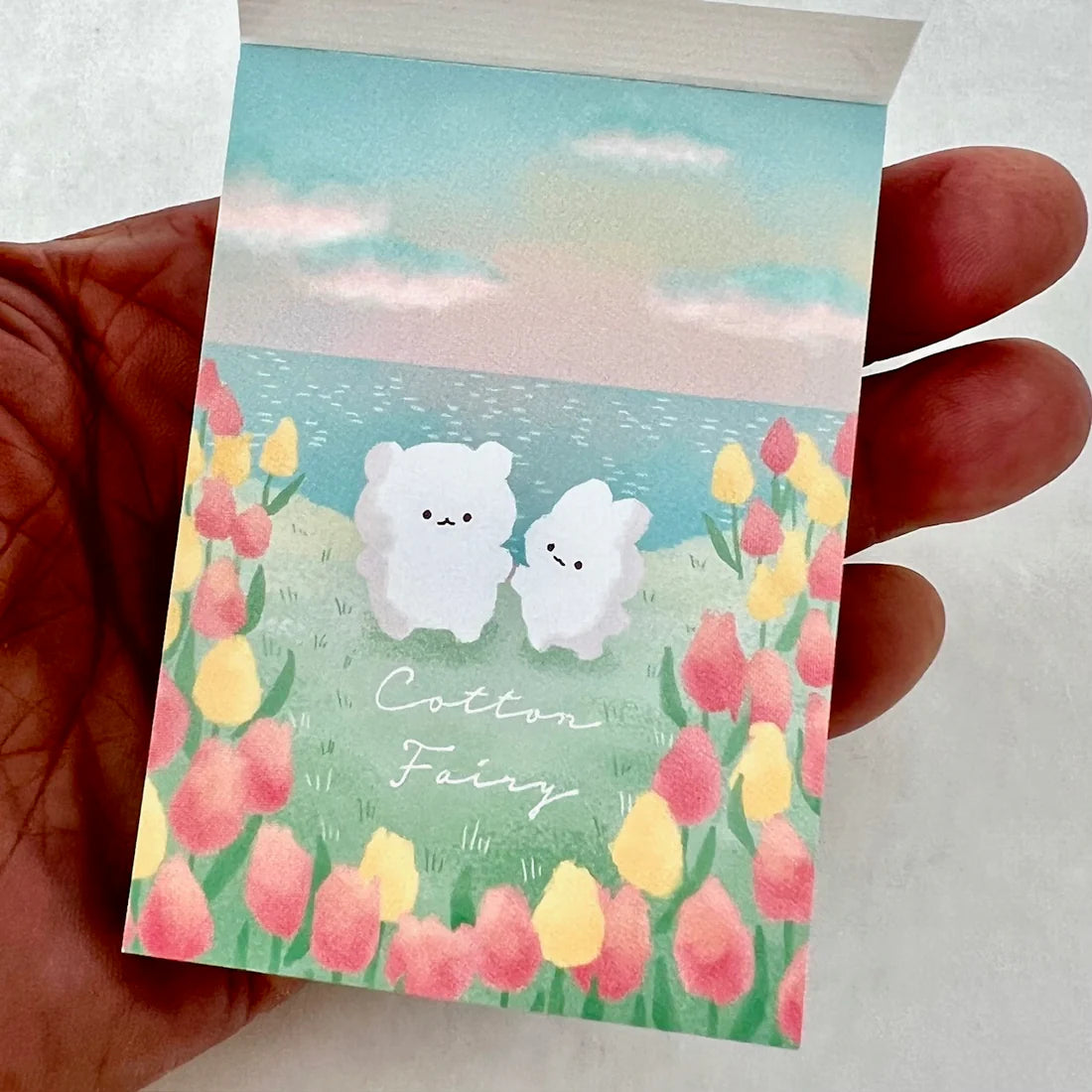 Mini Notepad | Cotton Fairy showing cute white characters with colorful flowers and ocean background in hand-held size.