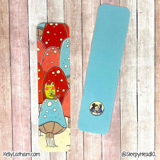 Frog & Mushrooms Bookmark showing a cute frog sipping juice atop colorful mushrooms with a solid blue back.