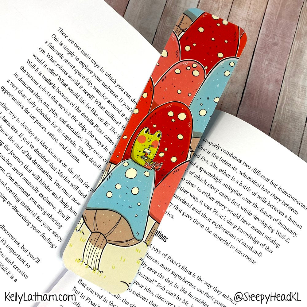 Frog & Mushrooms Bookmark featuring a cute frog drinking juice amid colorful mushrooms with glossy finish on thick paper.