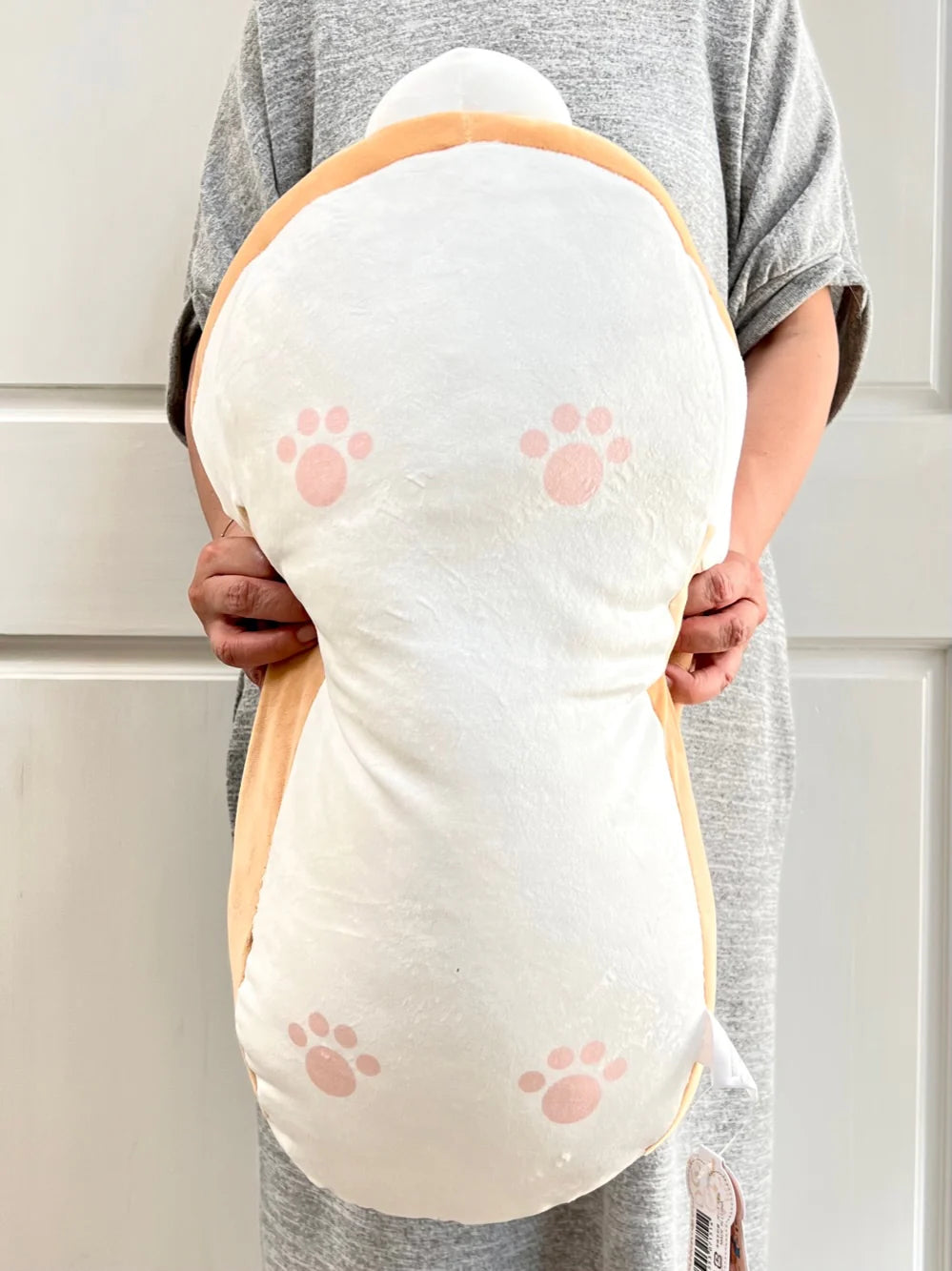 Person holding a soft and squishy Jumbo Long Dog plush pillow with cute pink toe beans.