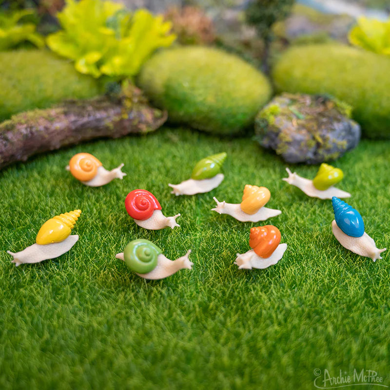 Itty Bitty Snails soft vinyl miniature snail toys in various colors arranged on green grass with moss and rocks.