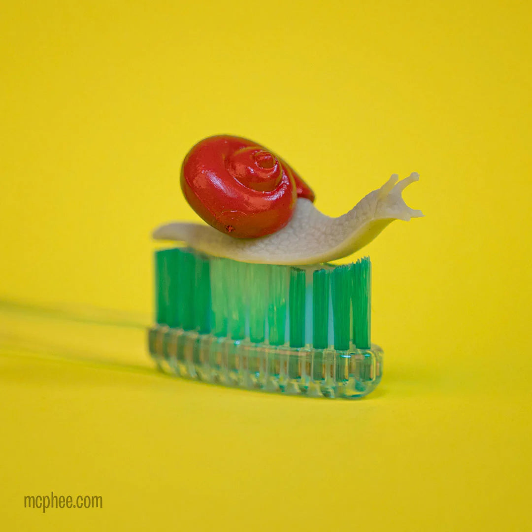 Itty Bitty Snails soft vinyl miniature snail with red shell perched on a green toothbrush against yellow background