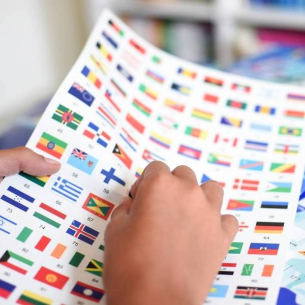 Hands placing stickers of world flags on a sheet for the Poppik Discovery Poster Flags educational geography poster.