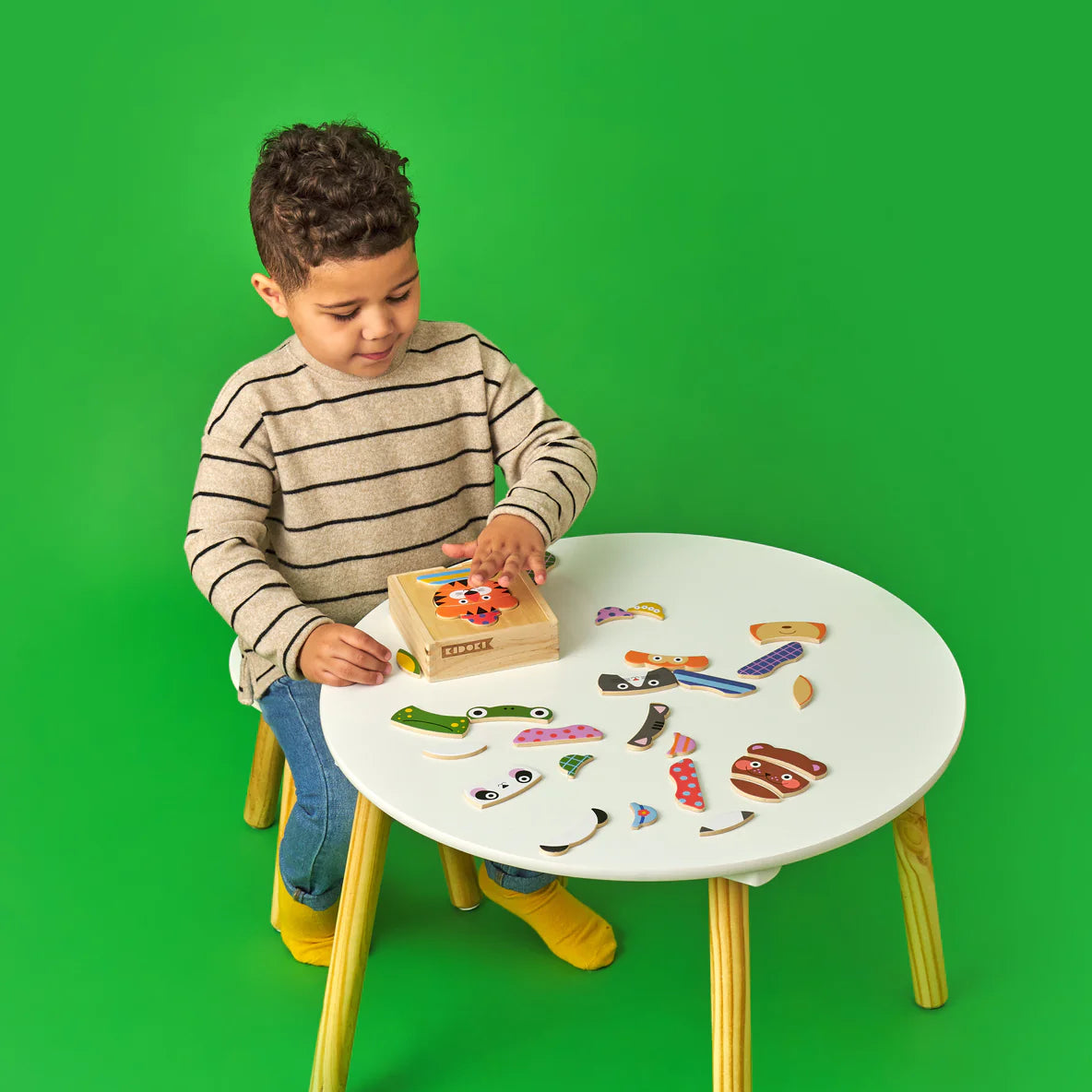 Child playing with Animal Mix Up! Wooden Puzzle pieces on a white table, creating unique animal face combinations.
