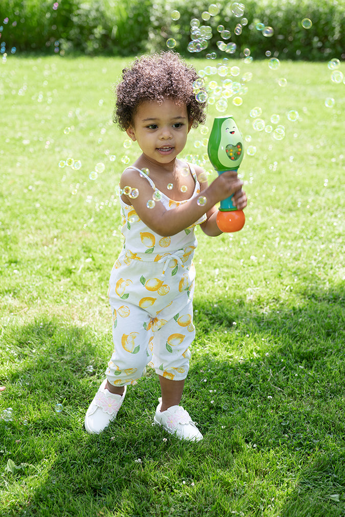 Toddler playing outdoors with Fisher Price No-Spill Shake & Go Bubble Maraca blowing bubbles on a sunny day.