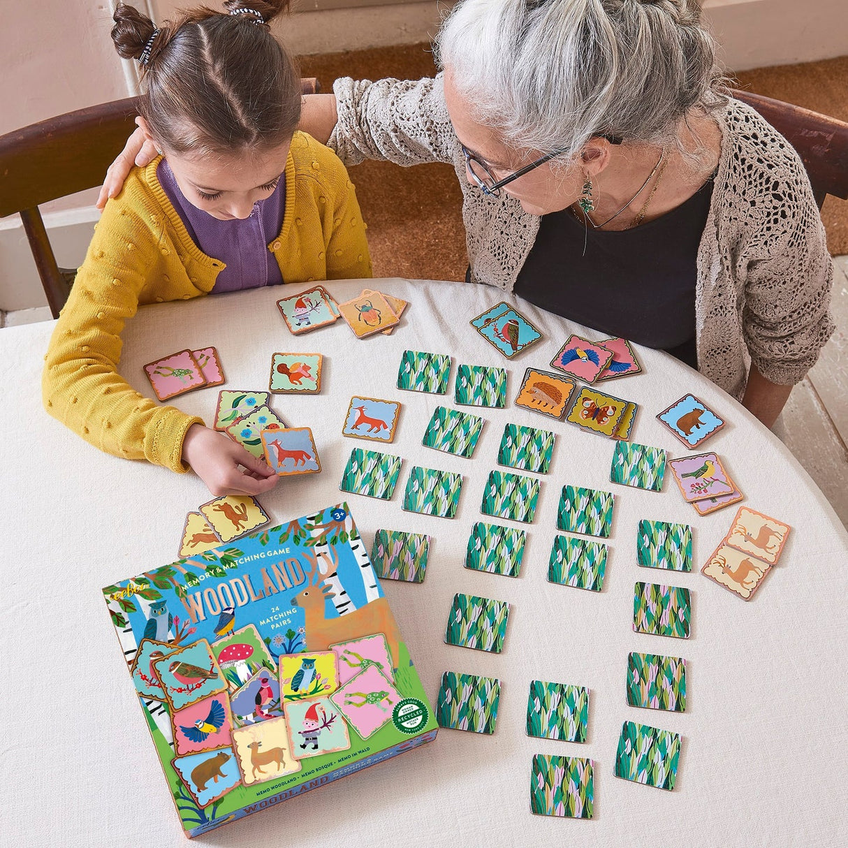 Memory & Matching Woodland game with illustrated animal cards and glossy copper gilding, played by child and elder at table.