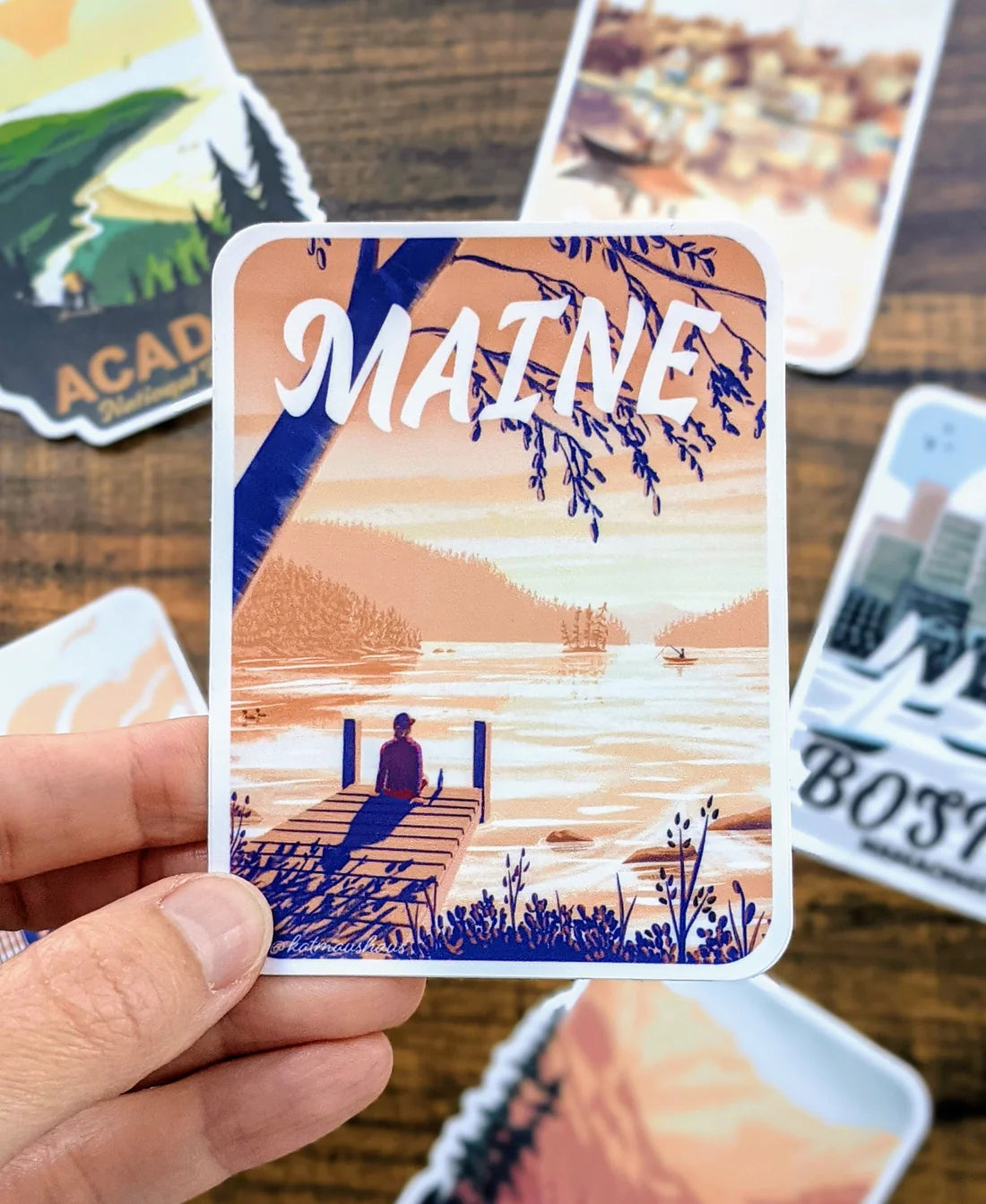 Maine Dock Sticker showing a peaceful lakeside scene with a person on a dock at sunset, durable and waterproof vinyl.