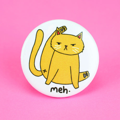 Meh Kitty Cat Button featuring a unimpressed cat grooming itself with "meh" text on a white round pin.