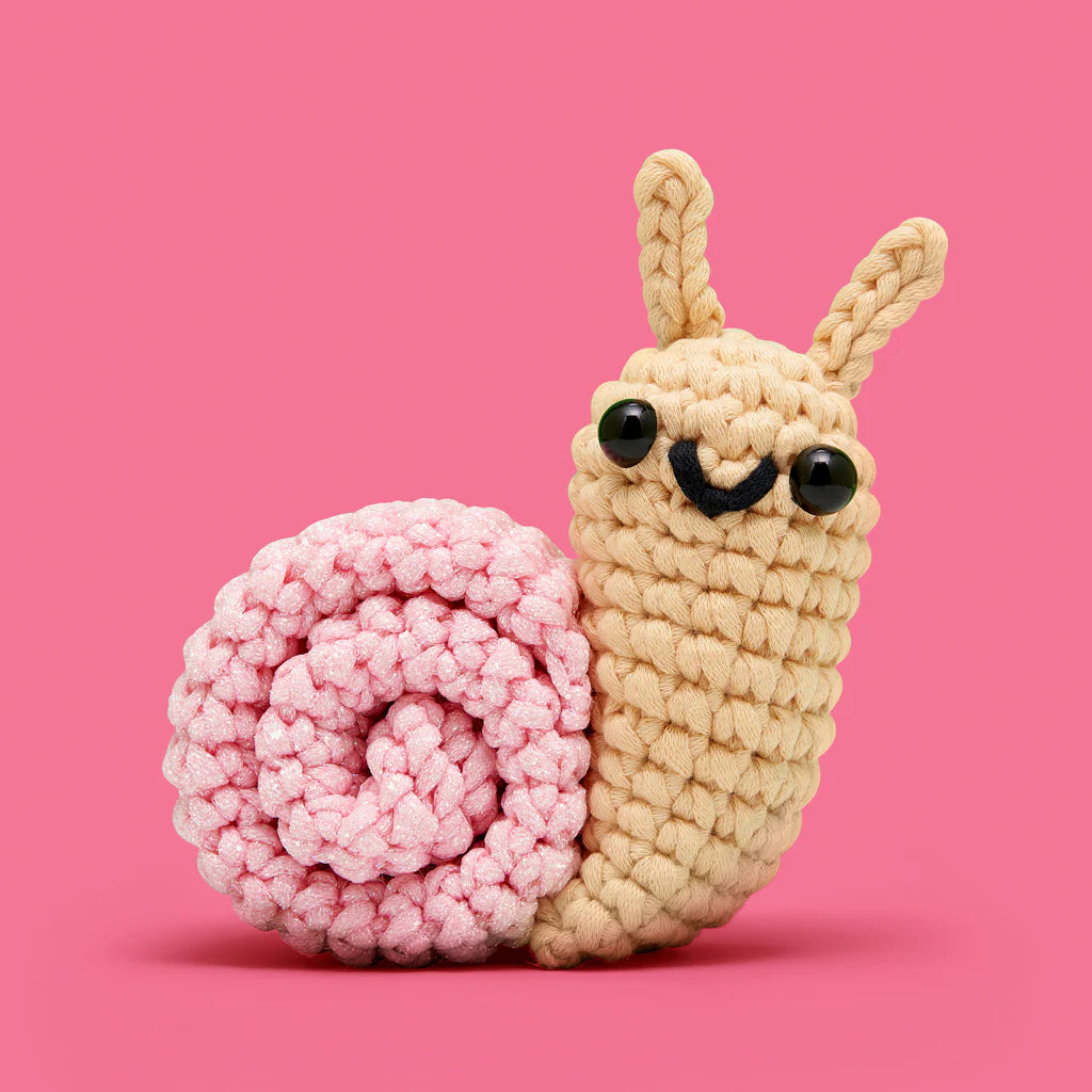 Cute crocheted snail with a soft pink shell and beige body against a bright pink background