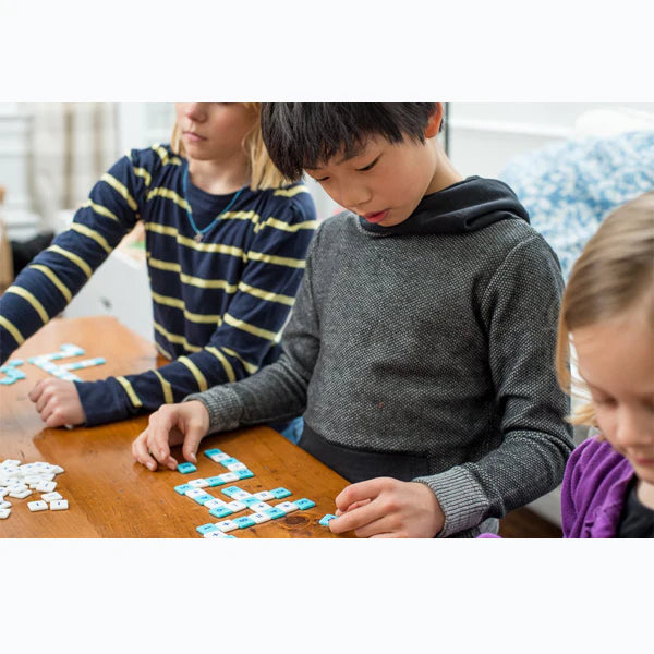 Children playing the Mobi Number Tile Game connecting math tiles in a crossword style grid on a wooden table.