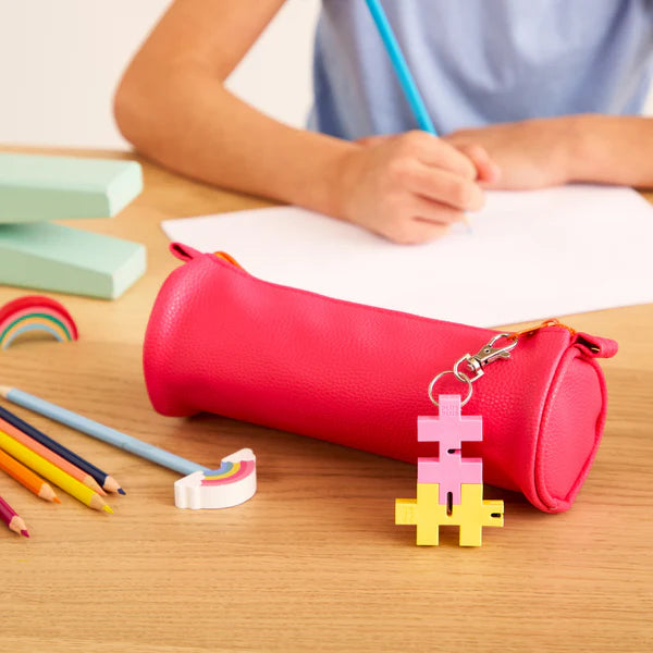 HEXEL Duo Keychain attached to a pink pencil case with colored pencils and a child writing in the background.
