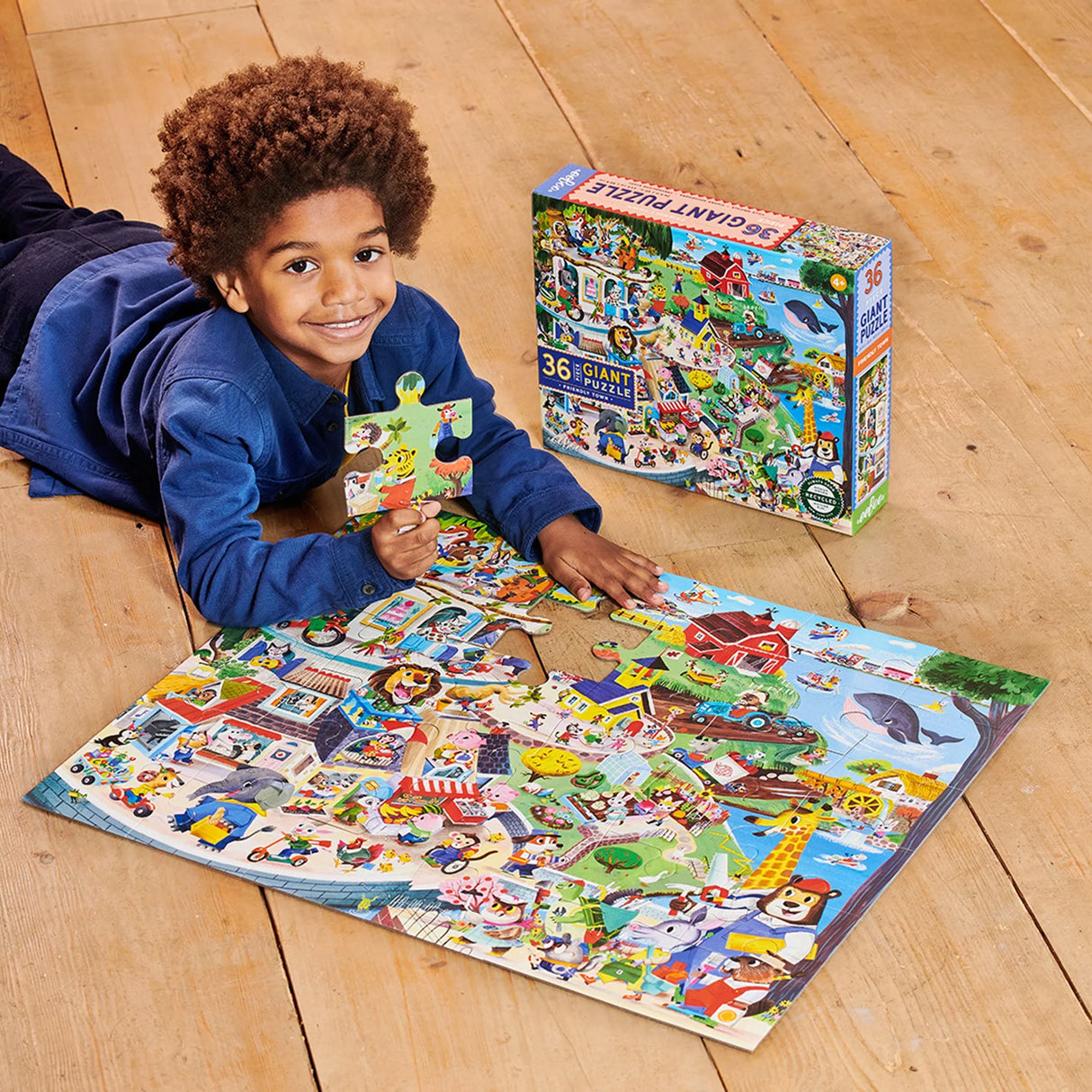 Child assembling colorful 36pc Friendly Town Giant Puzzle featuring friendly animals and community scenes.