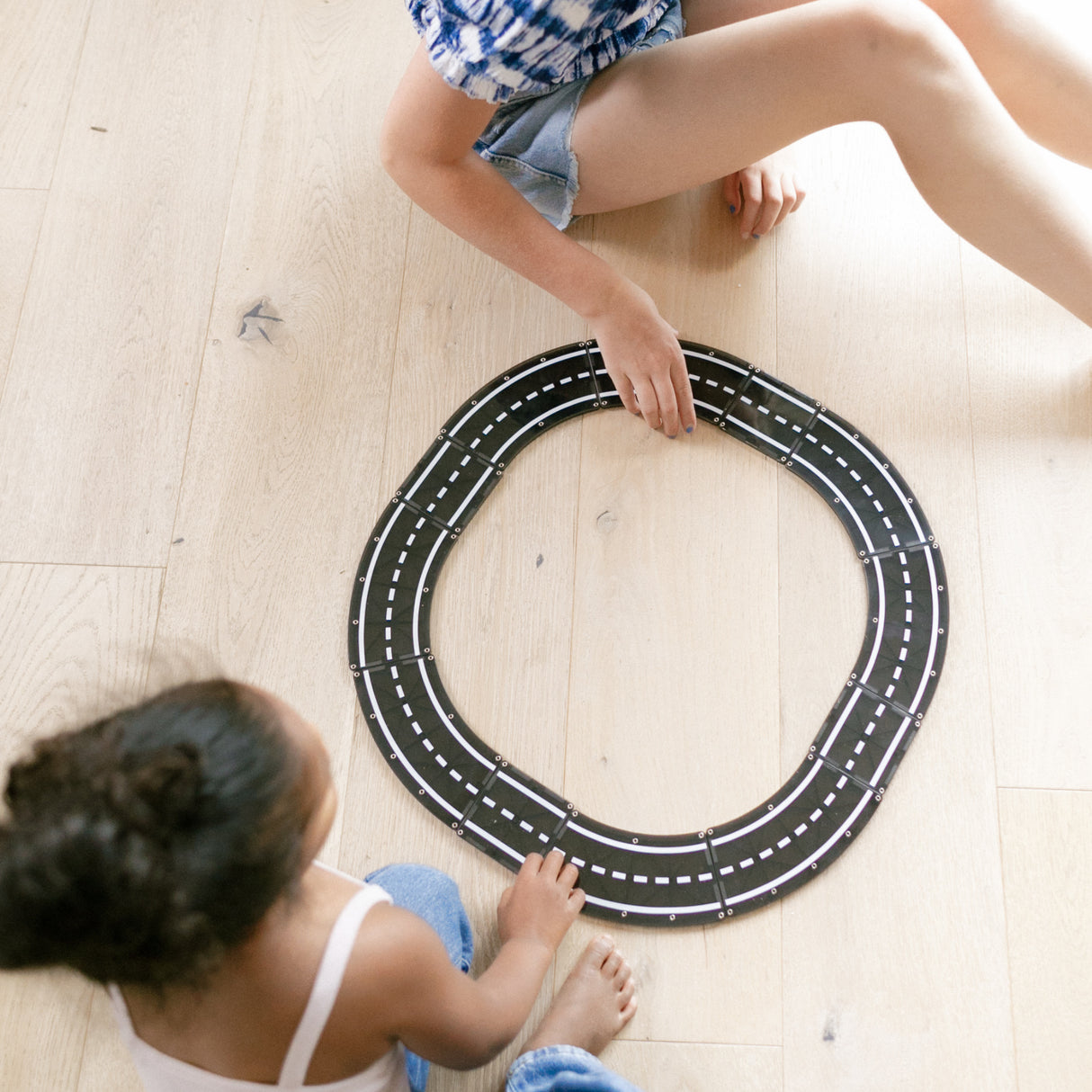 Children assembling Magnatiles Xtras Roadway 12pc magnetic road pieces into a circular track on a wooden floor.