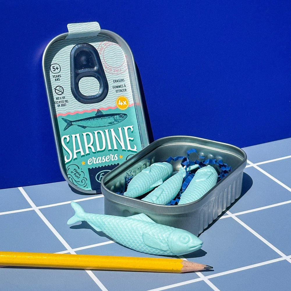 Set of four light blue sardine-shaped erasers in a metal tin on a grid surface next to a yellow pencil