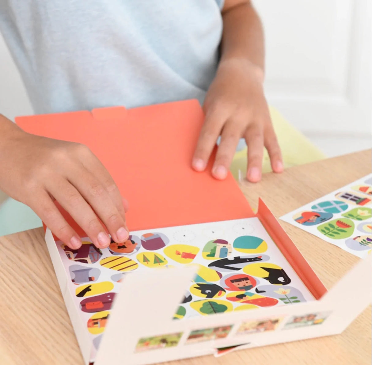 Child’s hands arranging colorful Poppik Sticker Story cards and stickers for a creative fairy tale activity.