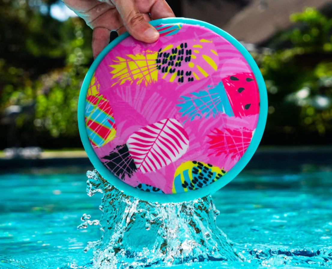 Hand holding colorful Waboba FLOBO Disc above water splashing, showing its floatable flying disc design.