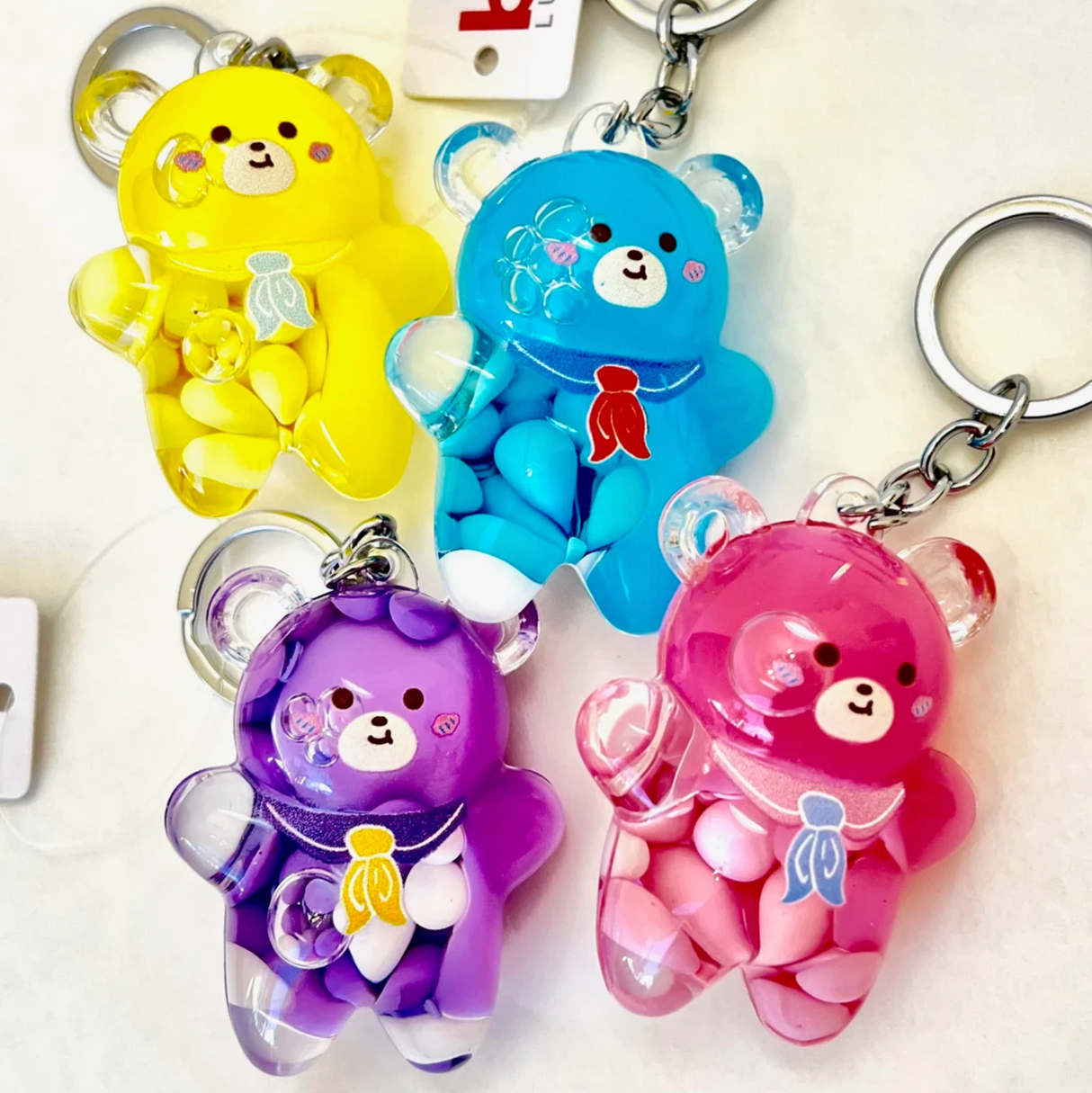 Four colorful Bear Floaty Charm Keychain toys in yellow, blue, purple, and pink with small candy inside and key rings attached.