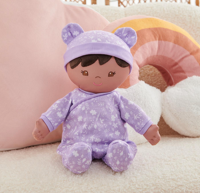 Recycled Baby Doll | Leilani in a soft purple floral onesie with embroidered features, made from 100% recycled materials.