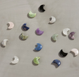 Carved Moon crystals in assorted types and colors, scattered on a light surface, showcasing their unique shimmer.