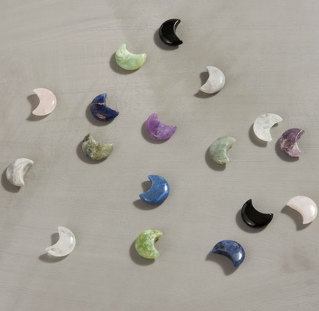 Carved Moon crystals in assorted types and colors, scattered on a light surface, showcasing their unique shimmer.