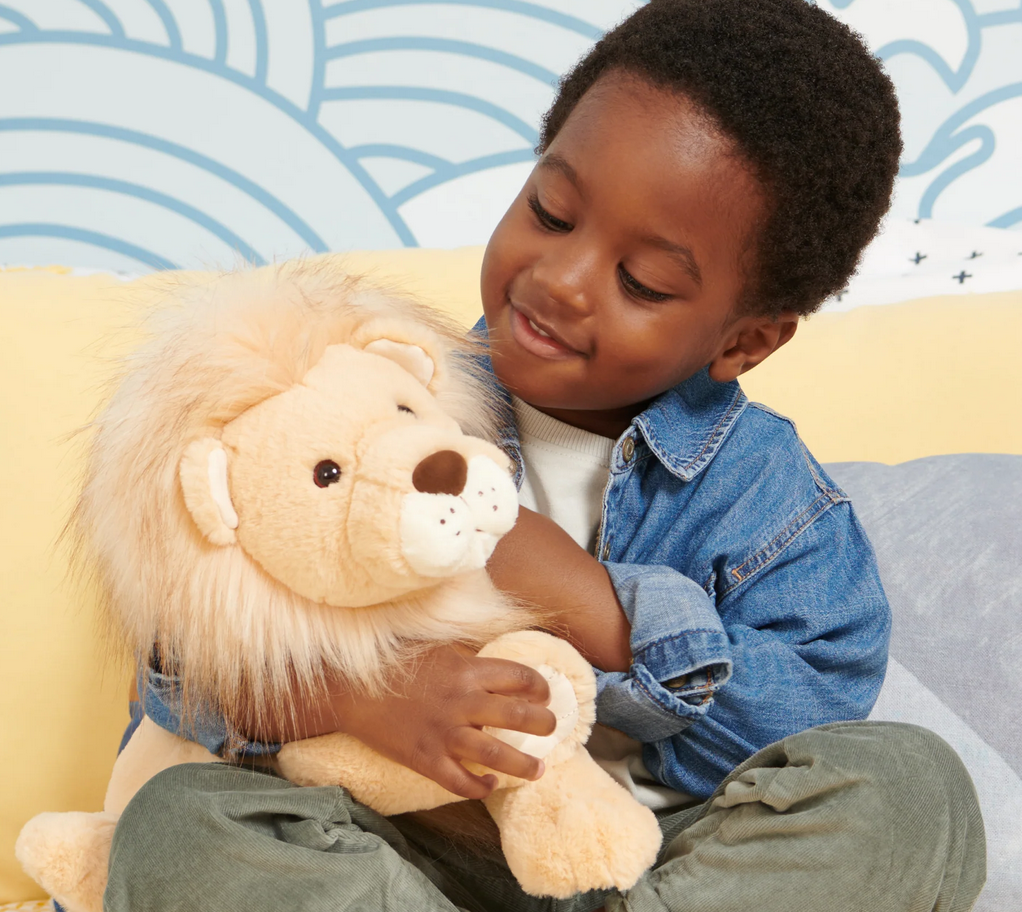 Child hugging the plush Lion Regis with a fluffy two-tone mane and soft tan fur in a cozy playroom.