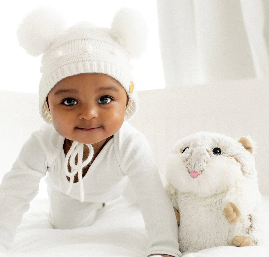 Baby dressed in white next to a plush Warmies | Hamster scented with real French lavender for soothing comfort.