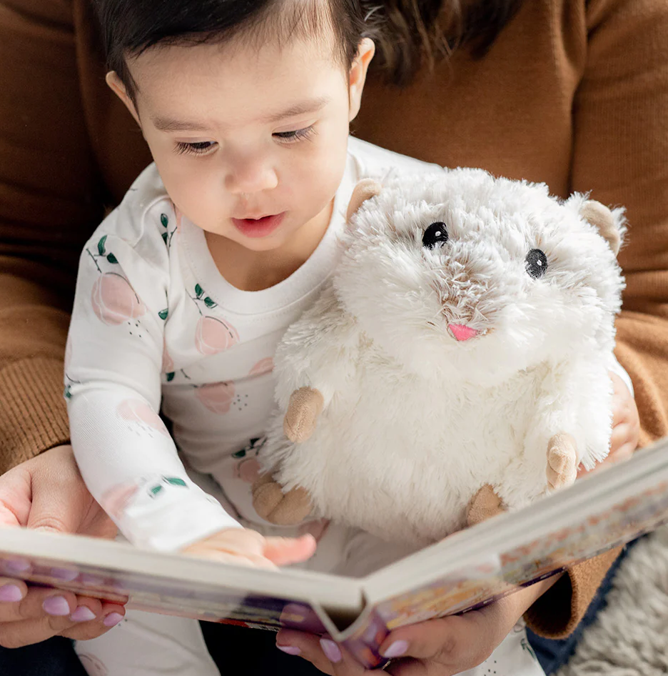 Child reading a book while holding a Plush Hamster Warmies scented with real French lavender for comfort.