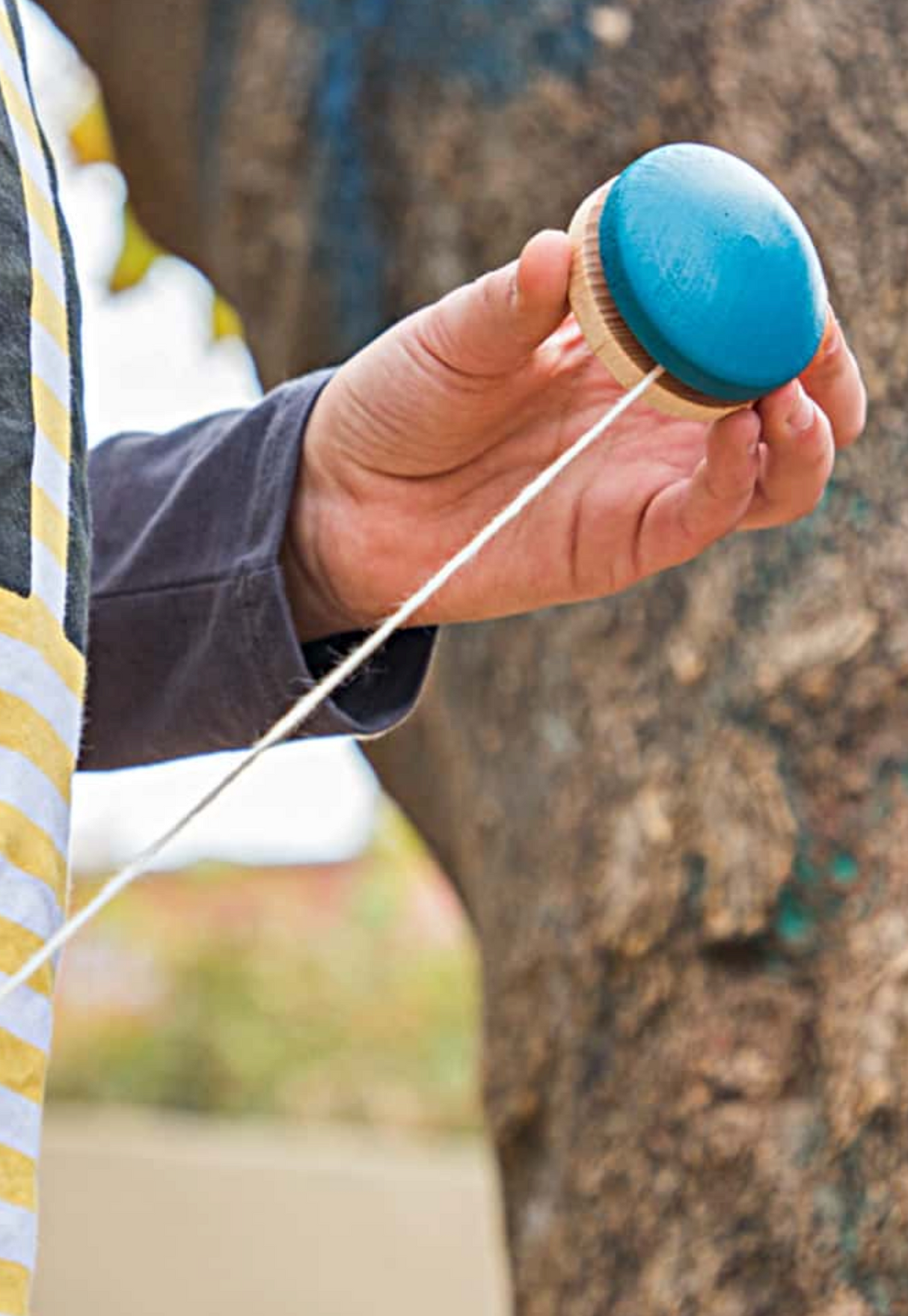 Hand holding a blue wooden yoyo with string outdoors, demonstrating play with Yoyo - Coral product.