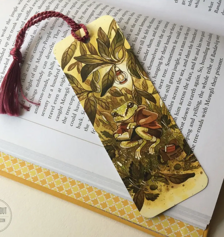 Bookmark Reading Treefrog with a Pacific Tree Frog reading under leaves and a burgundy tassel, 5.5 x 2 inches.