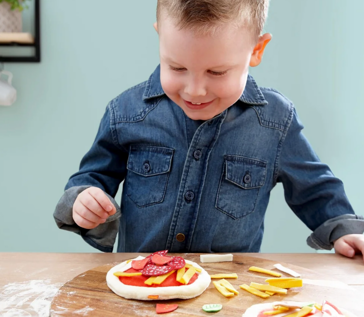 Young child playing with realistic toppings on a Mini Pizza toy for imaginative role-play and fun learning.