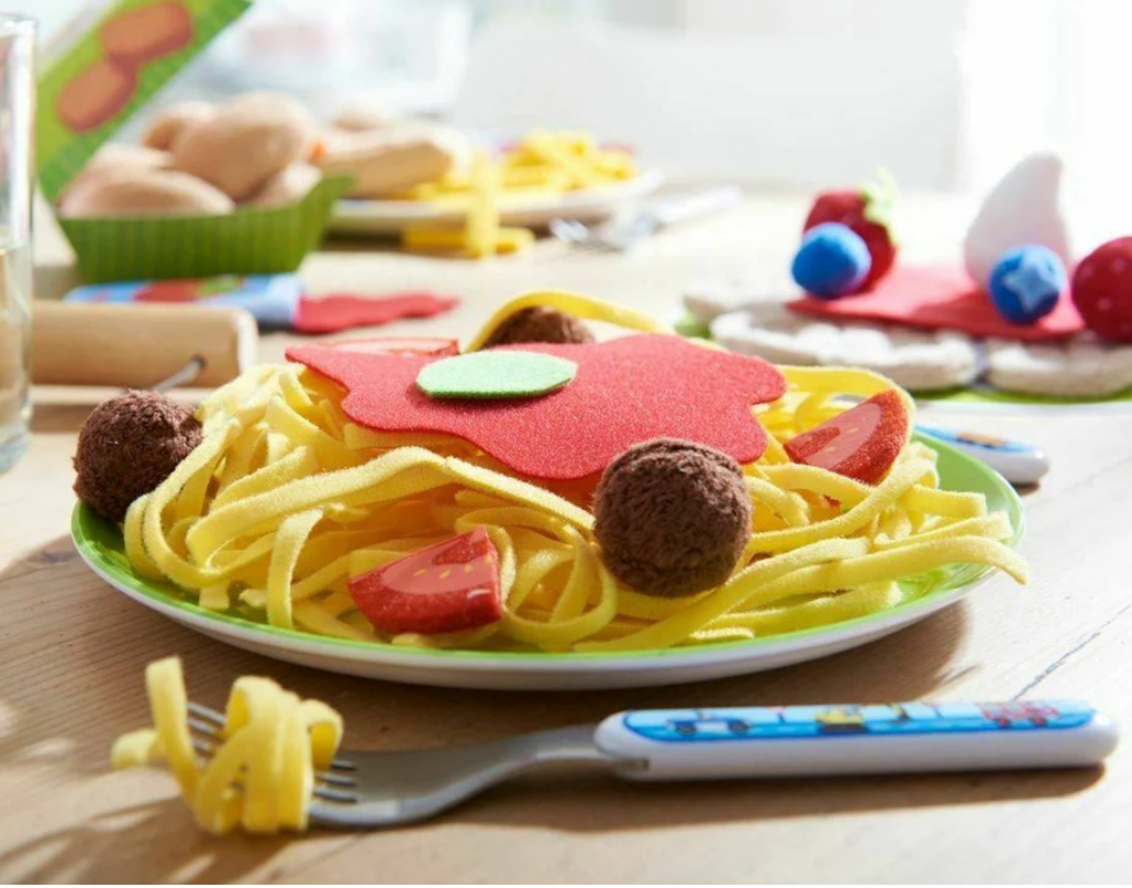 Spaghetti Bolognese play food set with noodles, meatballs, tomato wedges, and basil leaves on a green plate.