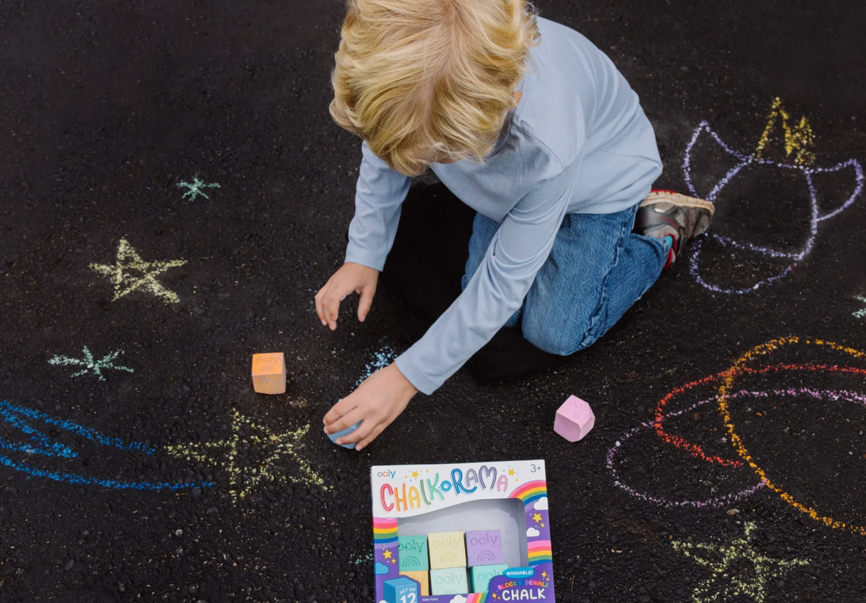 Child drawing colorful sidewalk art with Chalk-o-rama Block Sidewalk Chalk on black pavement outdoors.