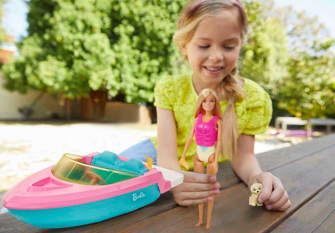 Barbie & Boat set with Barbie doll in pink vest, pet puppy, and colorful speedboat on wooden dock outdoors.