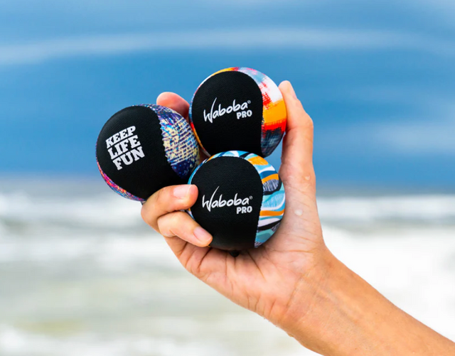 Hand holding three colorful Waboba Pro balls with ocean background, designed for advanced water play and control.