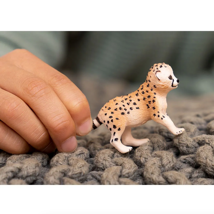 Hand holding a small, realistic Cheetah Cub toy on a textured gray surface, perfect for kids ages 3 and up.