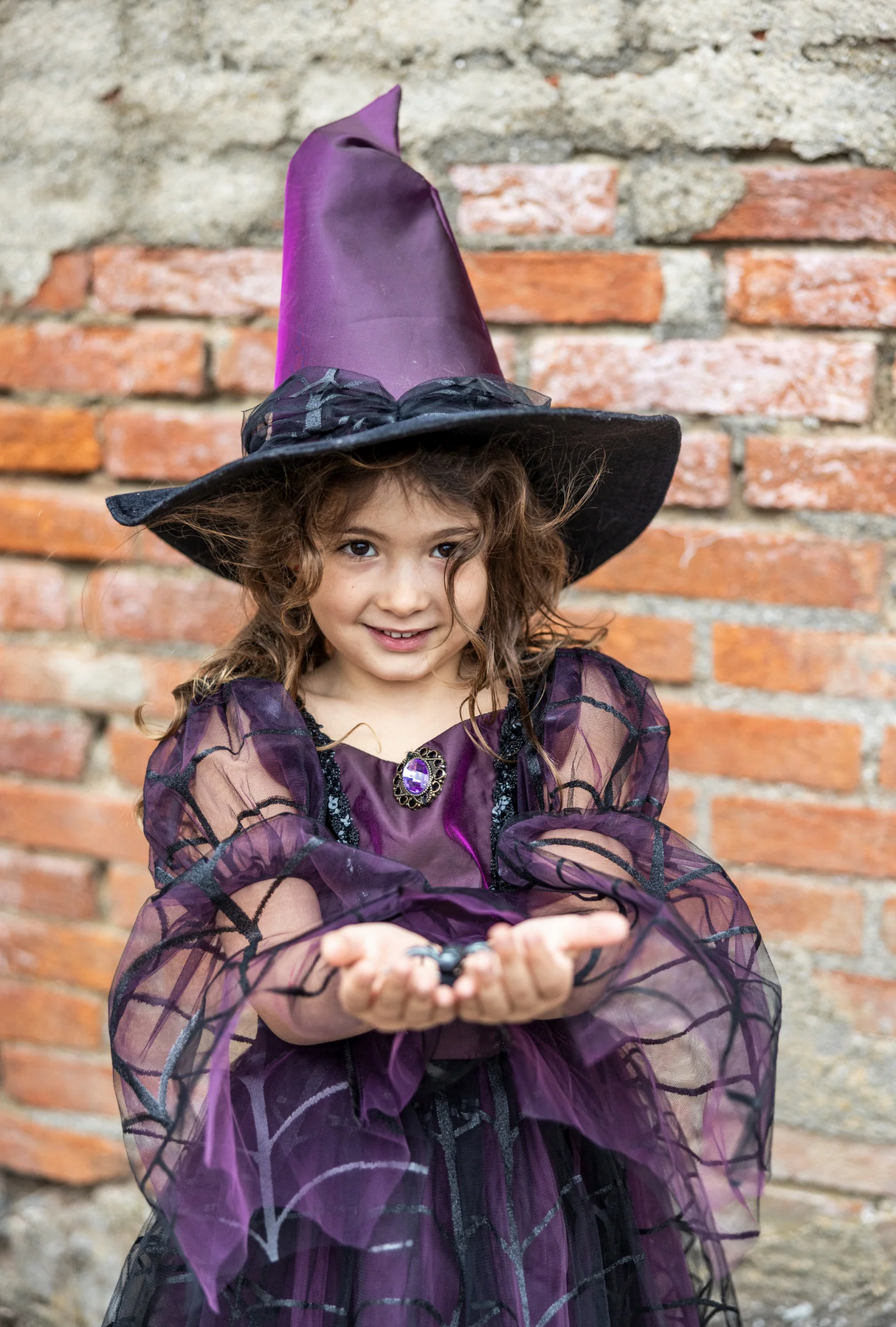 Child dressed in Amethyst the Spider Witch costume with purple hat and spiderweb dress posing outdoors.