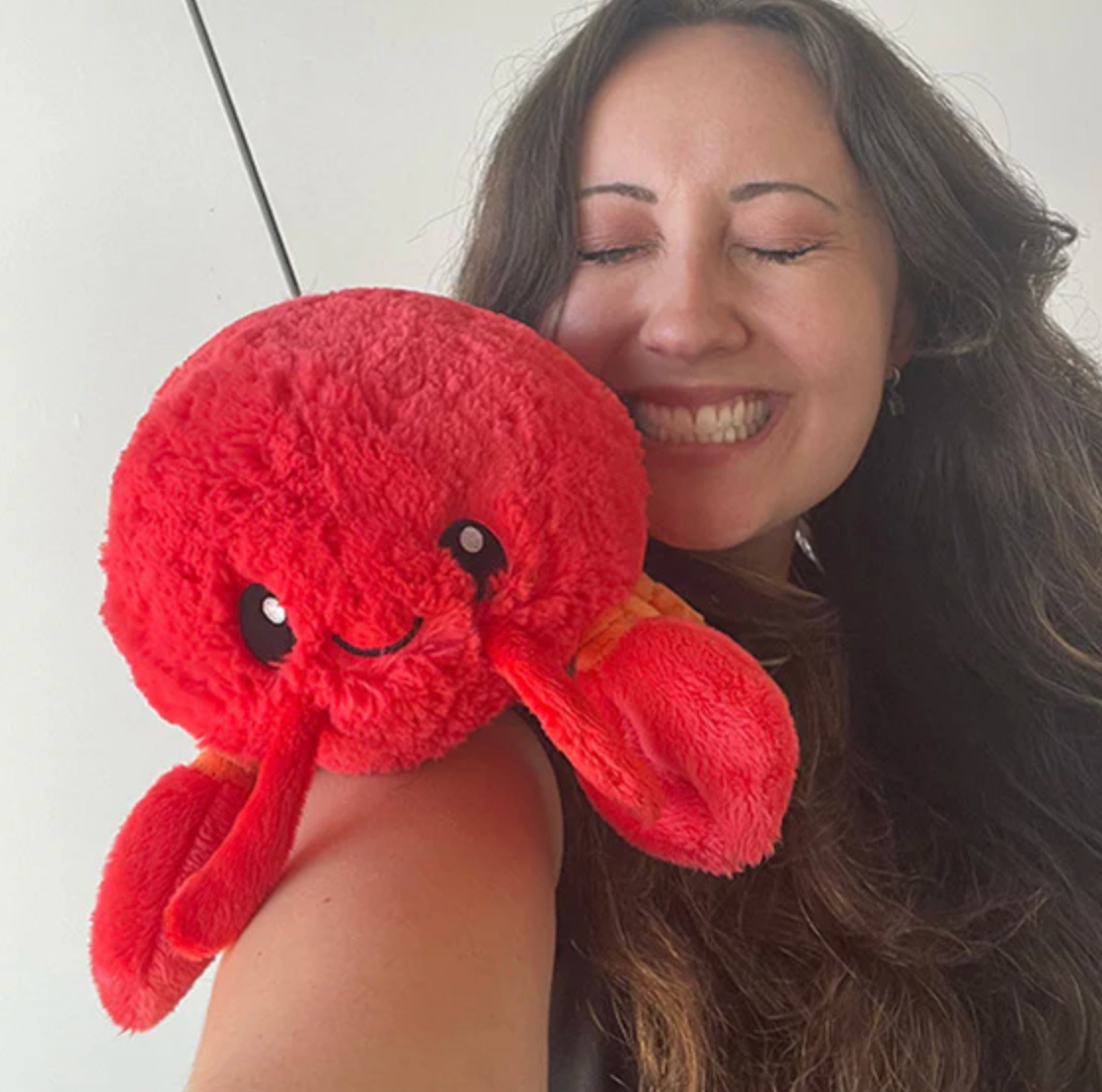 Smiling woman holding the bright red plush Lobster Mini toy made of soft polyester fiber.