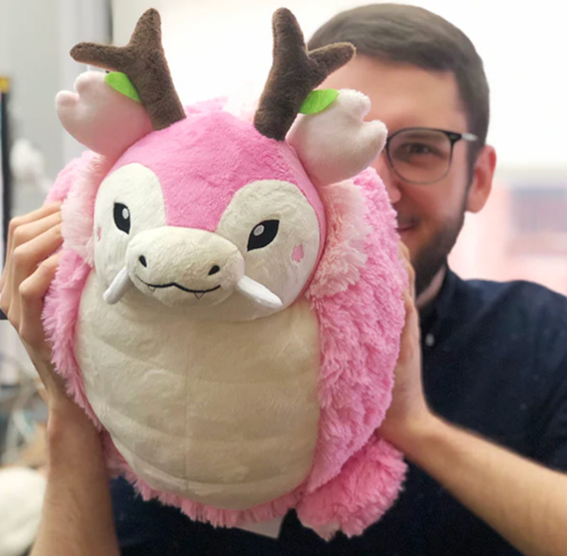Person holding a pink and cream plush Sakura Dragon toy with brown antlers and green leaves.