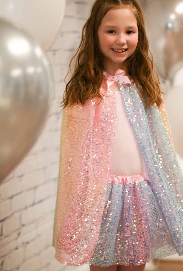 Young girl smiling wearing a shimmering Sequins Cape | Ombre Size 4-6 with pink, blue, and yellow hues.