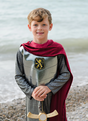 Young boy wearing the Silver Knight with Cape tunic with silver armor, red velour cape, and holding a sword by the beach.