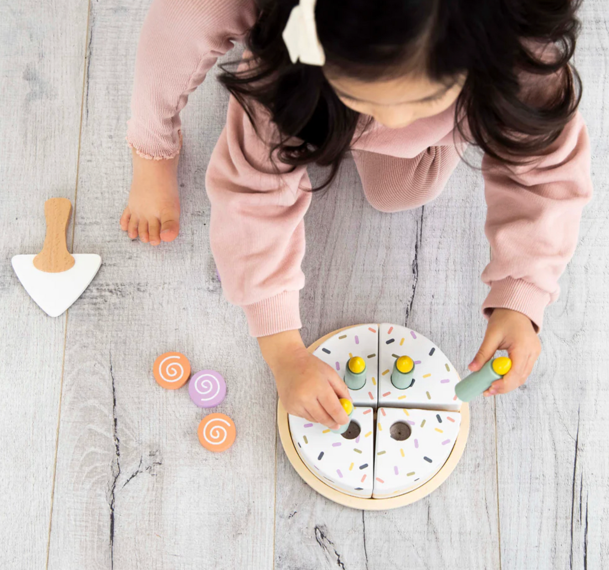 Child playing with the Celebration Wooden Cake Set, slicing and decorating the wooden frosted cake toy.