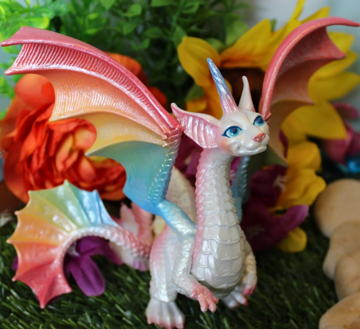 Fairy Rainbow Dragon figurine with pearlescent body and rainbow wings displayed on grass with colorful flowers background