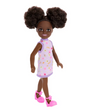 Barbie Chelsea #96 doll with curly space buns, purple floral dress, and pink star shoes, standing against white background.