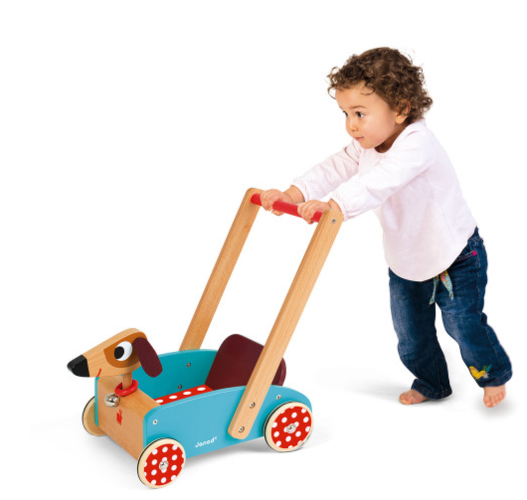 Child pushing a wooden Crazy Doggy Cart toy with felt ears and rubber wheels on a white background.